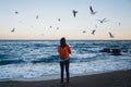 Young happy girl with orange backpack feeding seagulls on a seaside evening time Royalty Free Stock Photo