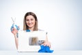 Young happy girl with scissors in her hands works at the sewing machine, on light blue background Royalty Free Stock Photo