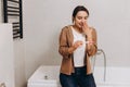 Young happy girl sitting in the bathroom and holding a positive pregnancy test in her hands. She is happy, covers her mouth with