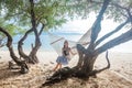 Young happy girl sitting in the hammock between green trees on the tropical beach Royalty Free Stock Photo