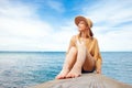 Young happy girl sitting on the pier barefoot and dreaming, woman in a sun hat resting Royalty Free Stock Photo