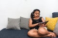 Young happy girl sitting on sofa using tablet listening to music with headphones