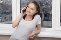 Young happy girl talking on the phone at home by the window, smiling, having fun