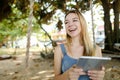 Young happy girl using tablet and riding swing on sand, wearing jeans sundress. Royalty Free Stock Photo