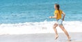 Young happy girl in a yellow T-shirt and shorts runs barefoot along the ocean, sea horizon and white waves on a sunny day, Royalty Free Stock Photo