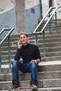 A young happy guy talking on mobile while sitting on the outdoor stairs. Royalty Free Stock Photo