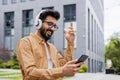 Young happy Hindu man dancing on the street wearing headphones, man using online application to listen to music and