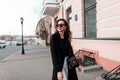 Young happy hipster woman in black sunglasses with a beautiful smile in fashionable spring clothes walks through the streets Royalty Free Stock Photo