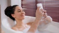 Young happy hispanic woman lying in hot comfortable foam luxurious bath relaxed girl typing sms on phone in bathroom