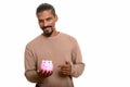 Young happy Indian man holding piggy bank and pointing finger Royalty Free Stock Photo