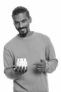 Young happy Indian man holding piggy bank and pointing finger Royalty Free Stock Photo
