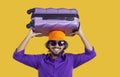 Young happy Indian man with tourist suitcase over head and sunglasses stands in yellow studio Royalty Free Stock Photo