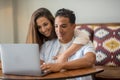 Young happy interracial couple boy and girl work and use together laptop computer at home sitting on the table. Modern online Royalty Free Stock Photo