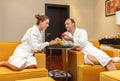 Young happy just married Caucasian couple in white bathrobes having fruits after spa on honeymoon. Man offers an apple to the Royalty Free Stock Photo