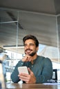 Young happy Latin business man in office holding phone looking away thinking. Royalty Free Stock Photo