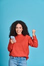 Young happy latin woman winner holding mobile cell phone isolated on blue. Royalty Free Stock Photo