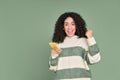 Young happy latin woman winner holding mobile cell phone isolated on green. Royalty Free Stock Photo