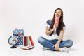 Young happy laughing woman student holding plastic cup of soda or cola drinking sitting near globe, backpack, school