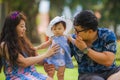 Young happy and loving Asian Chinese parents couple enjoying together with sweet daughter baby girl sitting on grass at green city Royalty Free Stock Photo