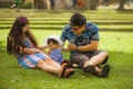 Young happy and loving Asian Chinese parents couple enjoying together with sweet daughter baby girl sitting on grass at green city Royalty Free Stock Photo