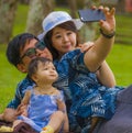 Young happy loving Asian Japanese family with parents and sweet baby daughter at city park together with father taking selfie pic Royalty Free Stock Photo