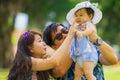 Young happy loving Asian Japanese parents couple enjoying together sweet daughter baby girl sitting on grass at green city park in Royalty Free Stock Photo