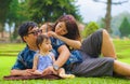 Young happy loving Asian Japanese parents couple enjoying together sweet daughter baby girl sitting on grass at green city park in Royalty Free Stock Photo