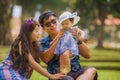 Young happy loving Asian Japanese parents couple enjoying together sweet daughter baby girl sitting on grass at green city park in Royalty Free Stock Photo