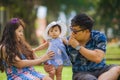 Young happy loving Asian Japanese parents couple enjoying together sweet daughter baby girl sitting on grass at green city park in Royalty Free Stock Photo