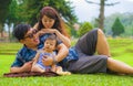 Young happy loving Asian Korean parents couple enjoying together sweet daughter baby girl sitting on grass at green city park in Royalty Free Stock Photo