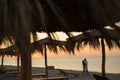 Young happy loving couple on the beach under straw umbrellas hugging and kissing at sunrise or sunset. Honeymoon. Royalty Free Stock Photo