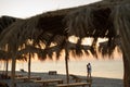 Young happy loving couple on the beach under straw umbrellas hugging and kissing at sunrise or sunset. Honeymoon. Royalty Free Stock Photo