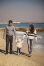 Young happy loving family with small kid in the middle, enjoying time at beach walking near ocean, holding arms, happy lifestyle f Royalty Free Stock Photo