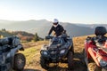 Young happy male driver in protective helmet enjoying extreme ride on ATV quad motorbike in fall mountains at sunset