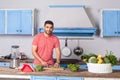Young man in casual t-shirt chopping cutting vegetables, preparing vegetarian salad in modern kitchen
