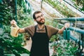 Young happy man gardener environmentalist holding a watering cans in hands, caring for plants in greenhouse Royalty Free Stock Photo