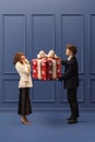 Young happy man giving present box to beautiful excited young girl against blue background. Christmas surprises Royalty Free Stock Photo