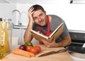 Young happy man at kitchen reading recipe book in apron learning cooking Royalty Free Stock Photo