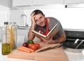 Young happy man at kitchen reading recipe book in apron learning cooking Royalty Free Stock Photo