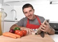 Young happy man at kitchen reading recipe book in apron learning cooking Royalty Free Stock Photo