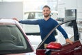 Young happy man leaning on car in dealership. Royalty Free Stock Photo