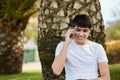 Young happy man sitting under tree talking on mobile Royalty Free Stock Photo