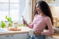 Young Happy Millennial Lady Using Smartphone And Drinking Tea In Kitchen Royalty Free Stock Photo