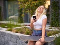 Young happy millennial woman sitting on a city street with headphones on her head - Teenager skateboarder girl listening to music Royalty Free Stock Photo