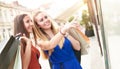 Young happy millennial women friends with colorful paper shopping bags looking on shopwindow - Right girl pointing on showcase - Royalty Free Stock Photo