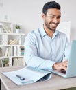 Young happy mixed race businessman working on a laptop alone in an office at work. One hispanic male boss smiling while Royalty Free Stock Photo