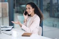 Young happy mixed race businesswoman on a call using her phone and desktop computer making a hand gesture in an office Royalty Free Stock Photo