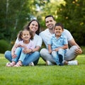 Young happy mixed race family relaxing and sitting on grass in a park together. Loving parents spending time with their Royalty Free Stock Photo