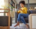 Young happy mixed race woman drinking a cup of coffee and typing a message on a phone at home. One content hispanic Royalty Free Stock Photo