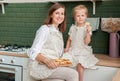 Young happy mom with her little daughter in the kitchen eating heart-shaped cookies. Home confectioner. Bakery